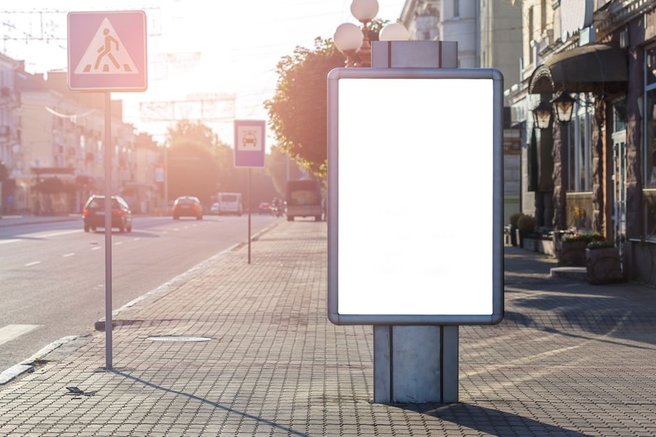 Anuncio en blanco sobre pasarela con edificio y señales viales en un día soleado
